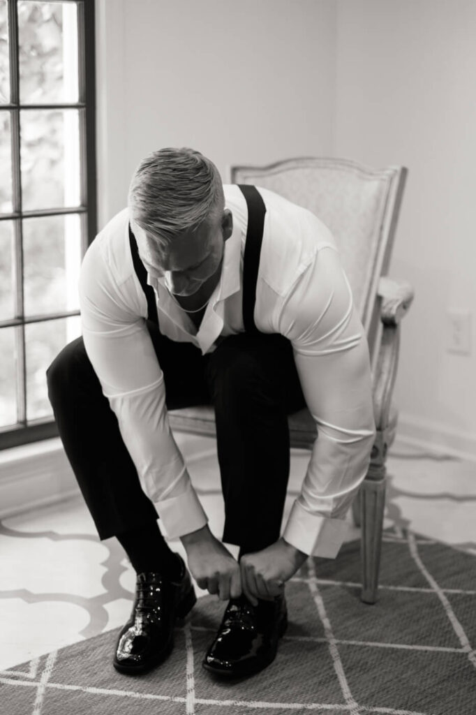 Groom laces up his shoes while getting ready for his Historic Robertson House wedding, captured in timeless black-and-white.