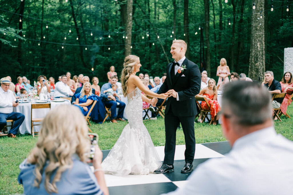 Bride and Groom's First Dance on Black and White Checkered Floor – The newlyweds share their first dance under twinkling string lights at their elegant outdoor wedding reception at The Historic Robertson House.