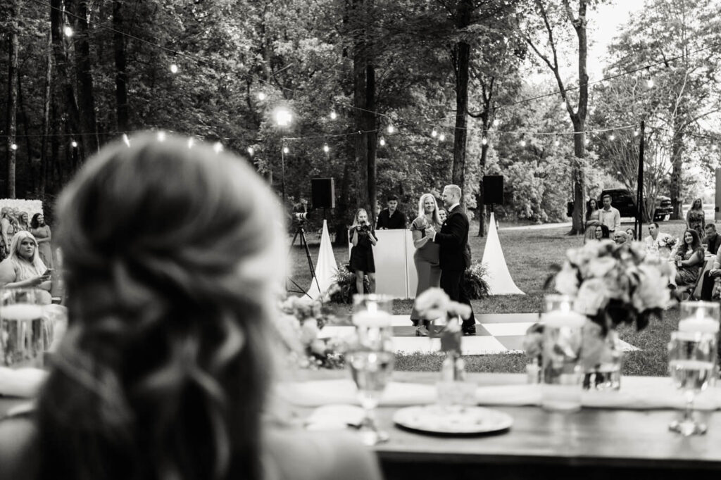 Mother-son dance under string lights – The groom shares a heartfelt dance with his mother on a black-and-white checkered dance floor, surrounded by guests and glowing lights at The Historic Robertson House.