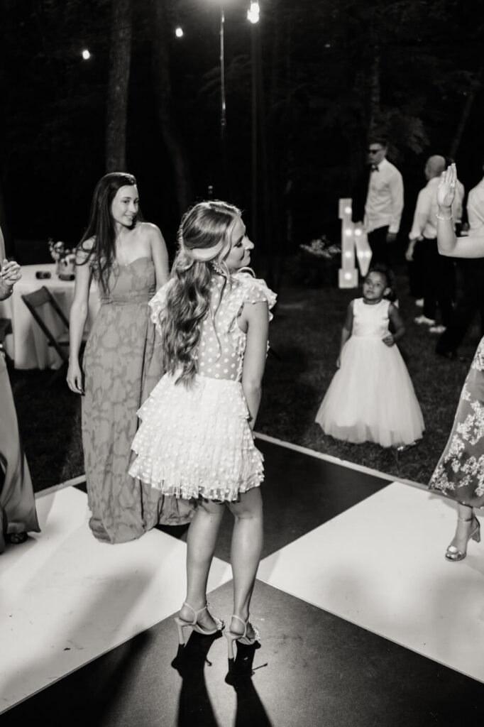 Bride dancing under the stars at her wedding reception – The bride twirls in her white polka-dot reception dress while guests and flower girls celebrate on the dance floor.