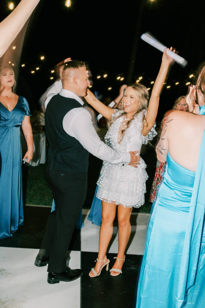 Bride and groom dancing joyfully at their wedding reception – The groom twirls the bride on the dance floor as she throws her hands up in excitement, surrounded by wedding guests in a lively celebration.