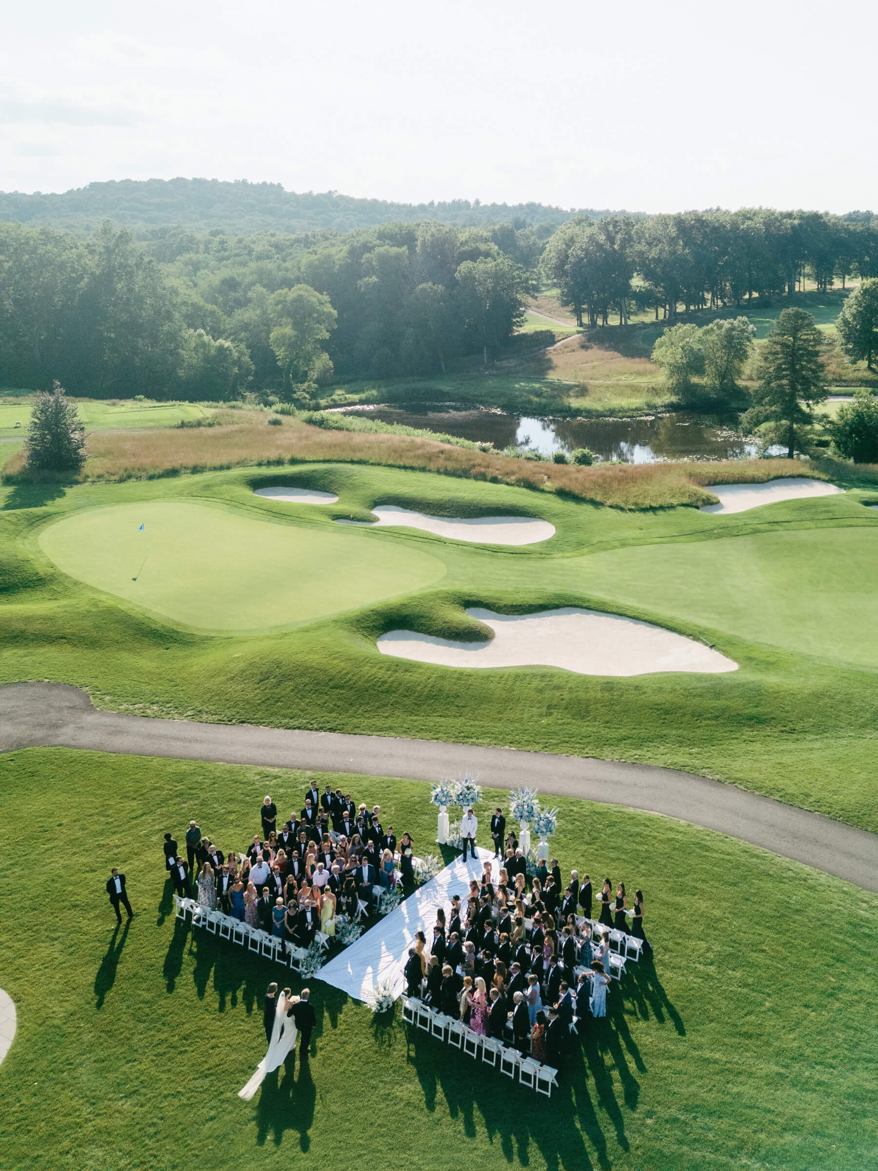 Aerial view of an outdoor wedding ceremony at Bedford Golf & Tennis Club, with guests seated on the lawn surrounded by rolling green fairways during a New York country club wedding