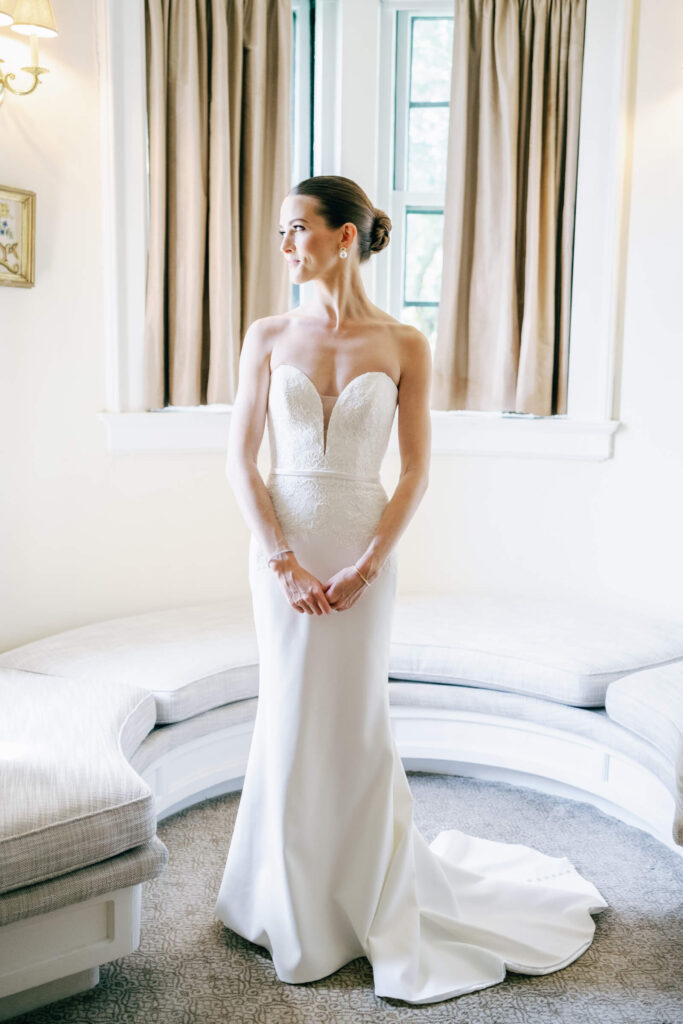 Portrait of the bride in her strapless lace wedding gown, standing elegantly in the Castle Hotel & Spa suite during her New York country club wedding morning