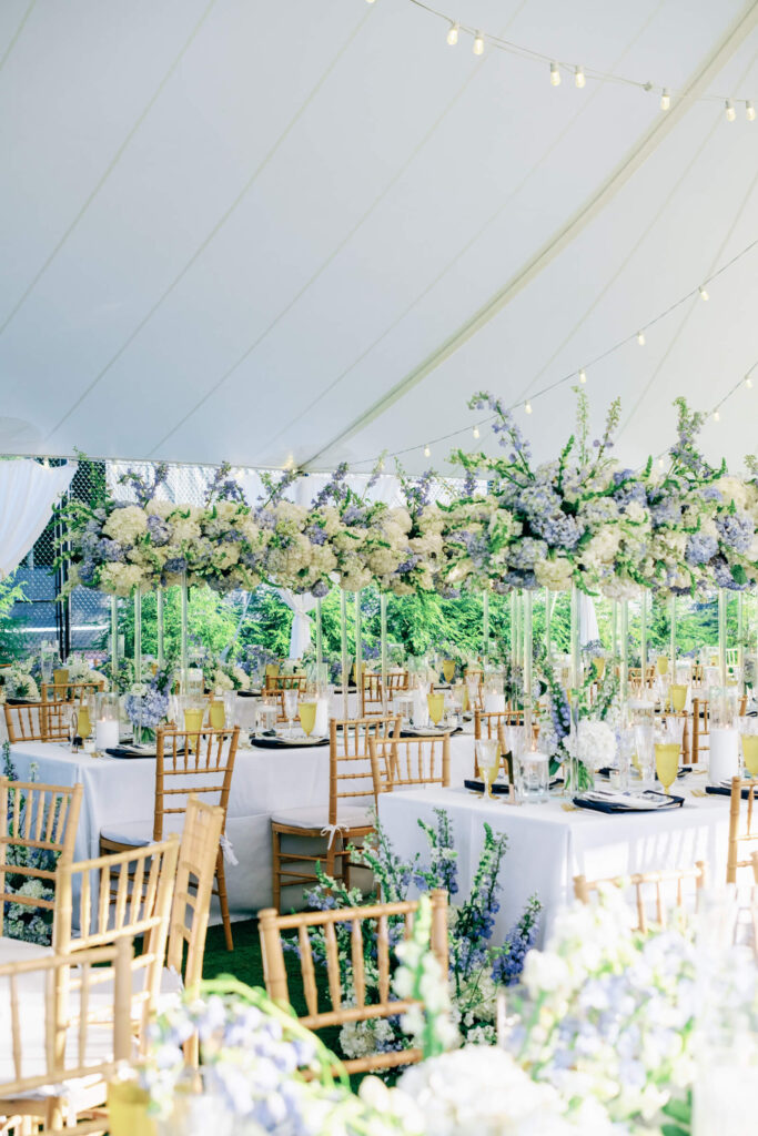 Full view of floral installations and rows of reception tables under a white sailcloth tent with string lights at a Bedford wedding