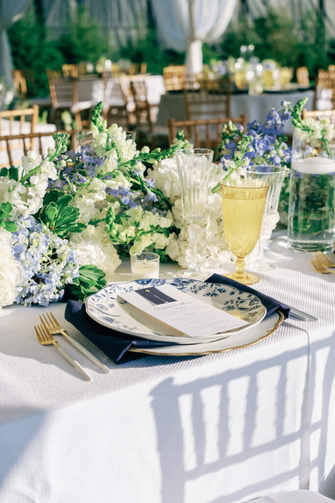 Place setting featuring blue floral china, navy napkins, and crystal glassware surrounded by white and blue florals