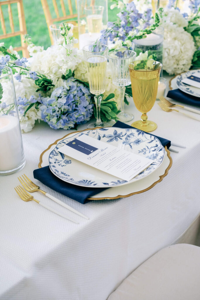 Table setting showing clear and amber glassware, blue floral charger plate, and romantic candlelight surrounded by soft blooms