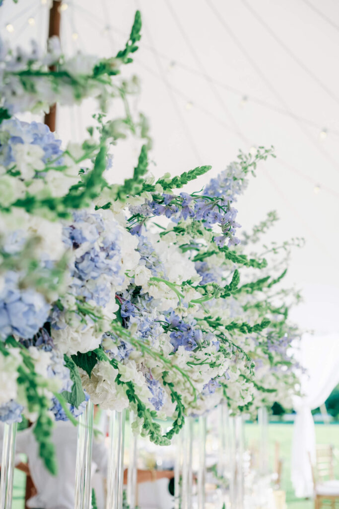 Close-up of dreamy white and blue wedding florals with delphiniums, hydrangeas, and snapdragons under a sailcloth tent ceiling