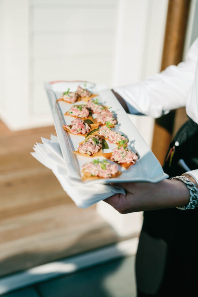 Waitstaff holding a tray of passed appetizers—mini tartare bites on crisps—during cocktail hour at a luxury outdoor wedding.