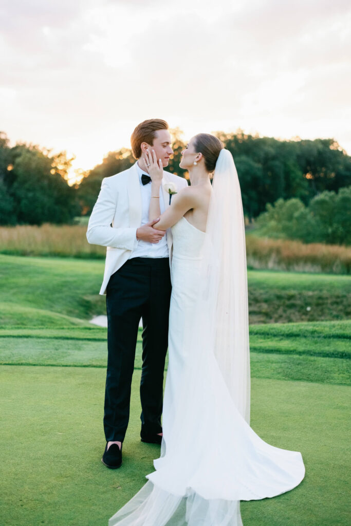 Bride and groom share an intimate moment on the green, gazing into each other’s eyes during golden hour.