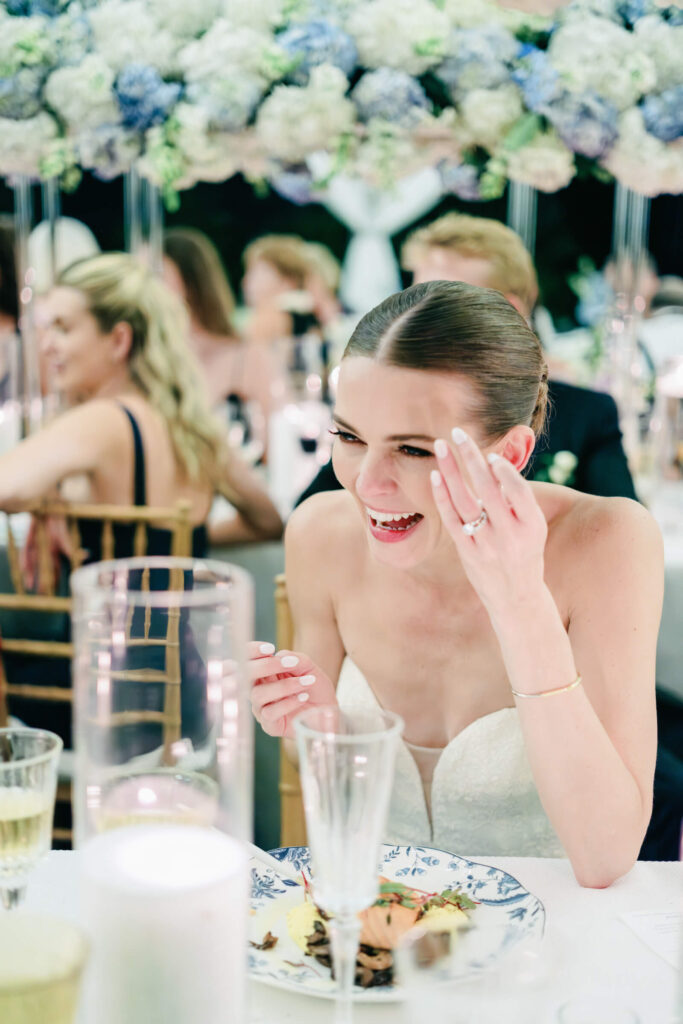 Bride laughing joyfully at the reception dinner, surrounded by friends and elegant floral centerpieces