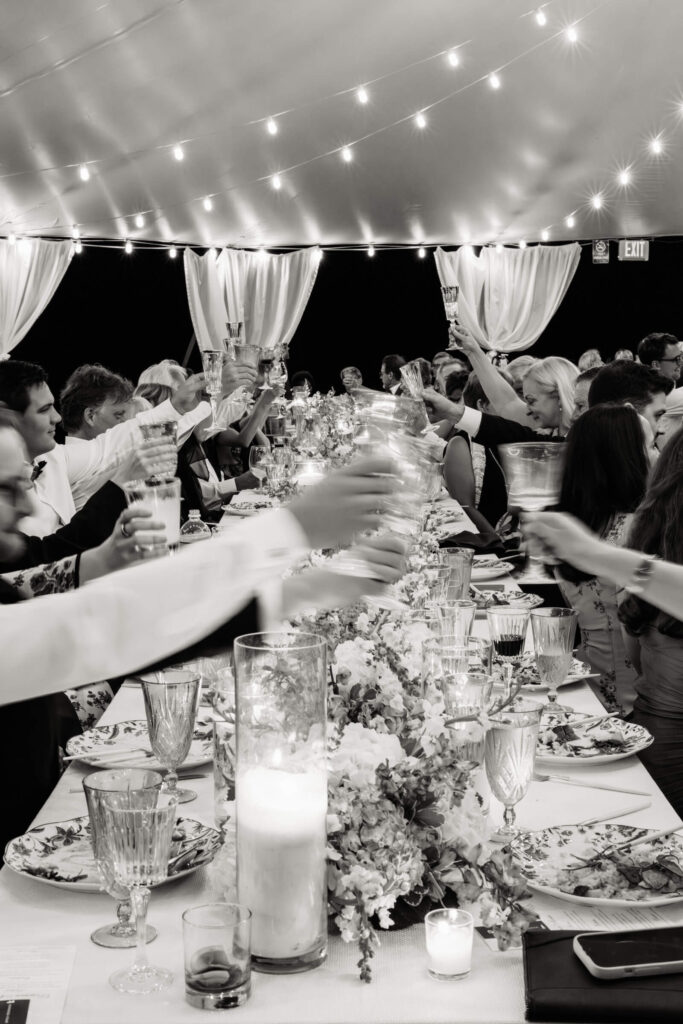 Guests raising glasses in a joyful toast under a canopy of string lights during the reception dinner.