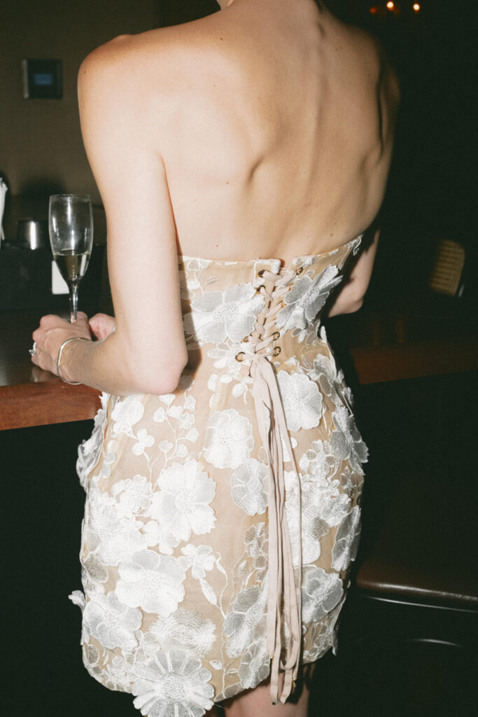 Back detail of bride’s floral lace mini dress showing the corset-style lacing