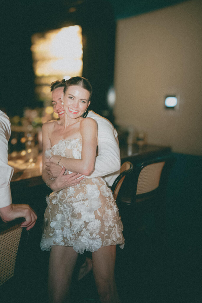 Bride laughing in the groom’s arms at the bar during the after-party