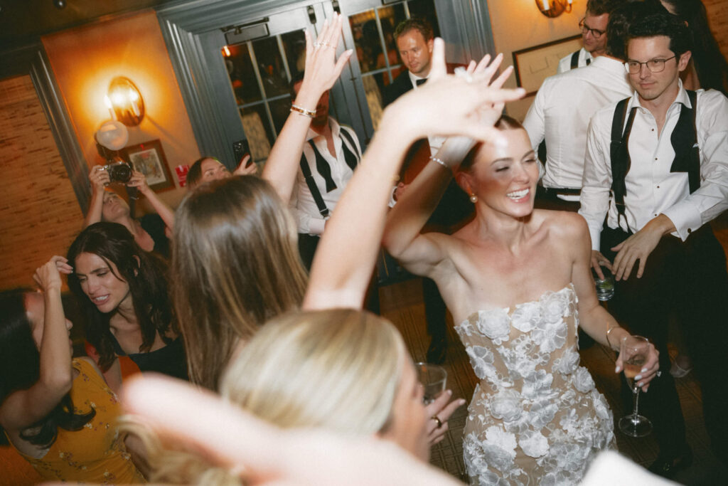 Bride dancing joyfully among guests at the after-party, hands raised in celebration