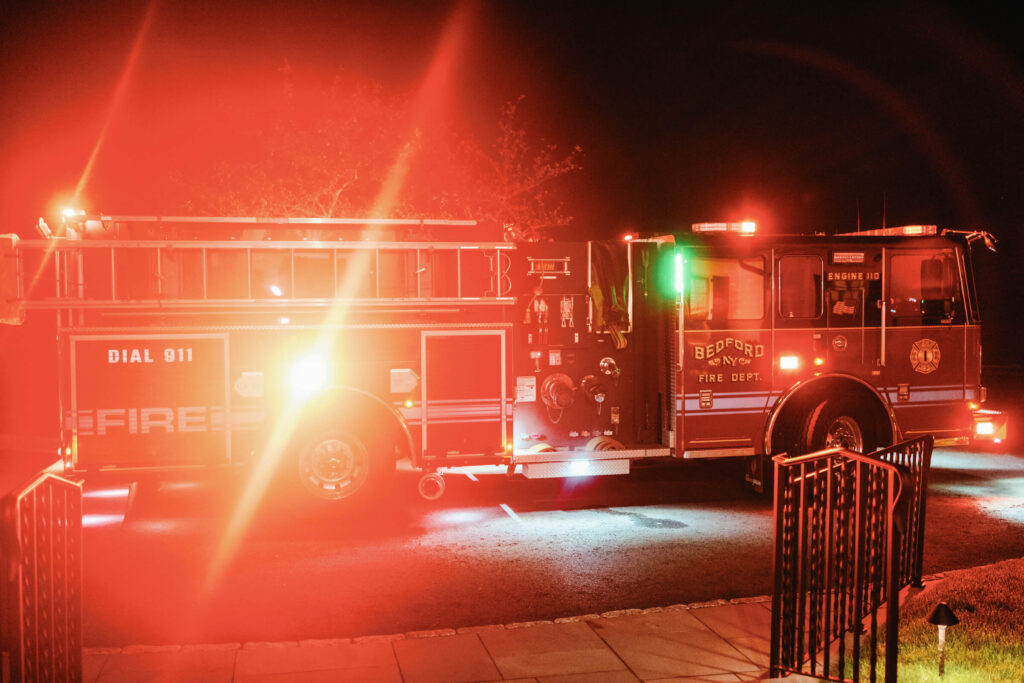 A Bedford, NY fire truck parked outside the venue at night with flashing red emergency lights.