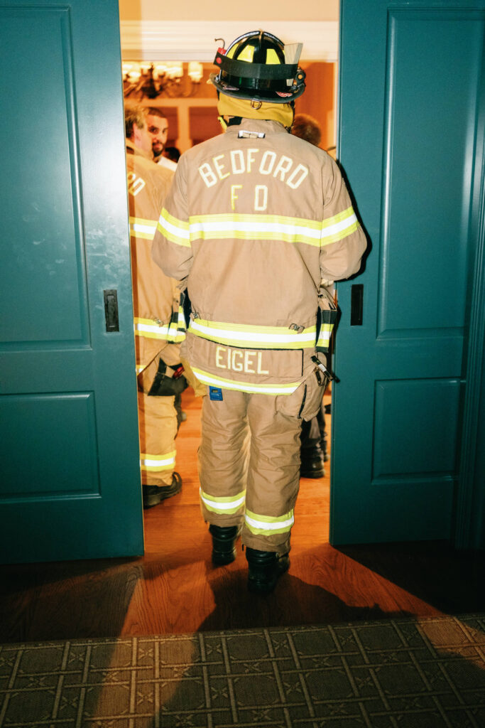 Firefighter in full gear walking through a doorway into the venue, with "BEDFORD FD" on the back of their jacket.