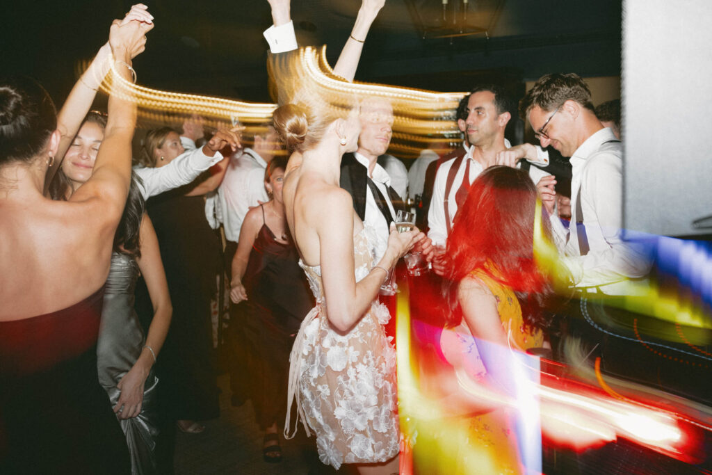 Guests dancing enthusiastically with vibrant motion blur and colorful lighting streaks during the reception.