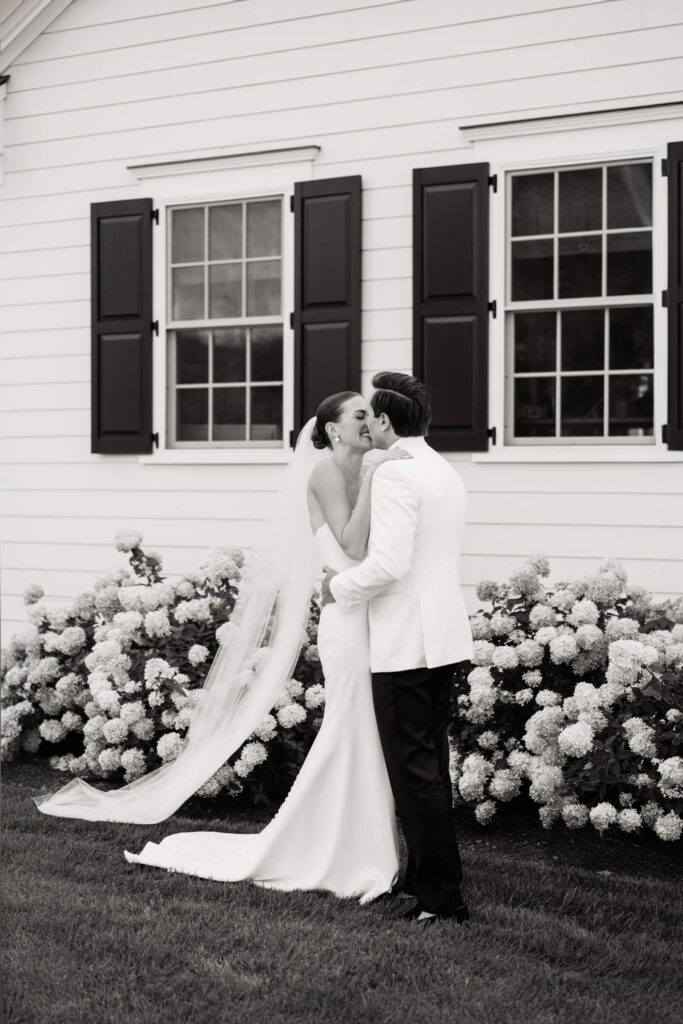 Bride and groom kiss during first look surrounded by white hydrangeas at New York country club wedding