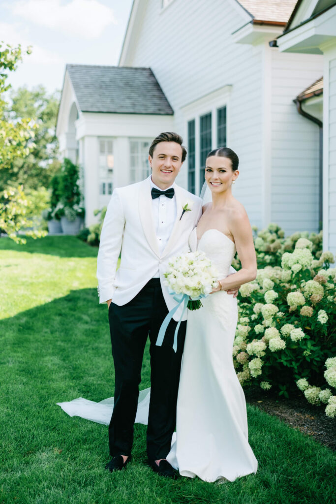 Bride and groom pose together in front of white hydrangeas at Bedford Golf & Tennis Club wedding