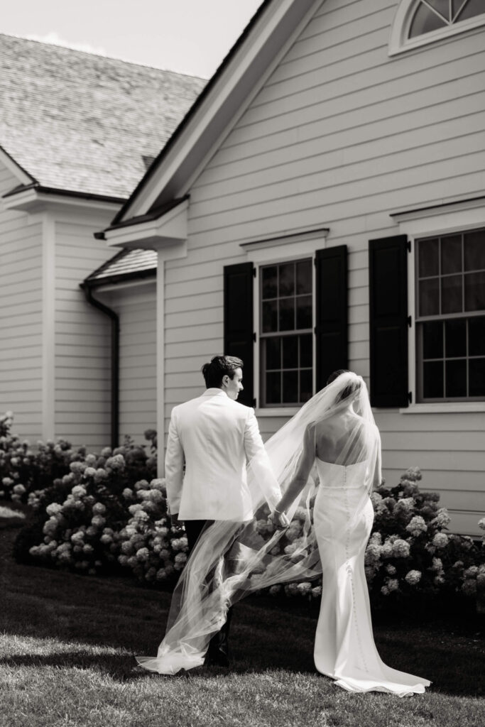 Black and white photo of bride and groom walking away from Bedford Golf & Tennis Club hand-in-hand