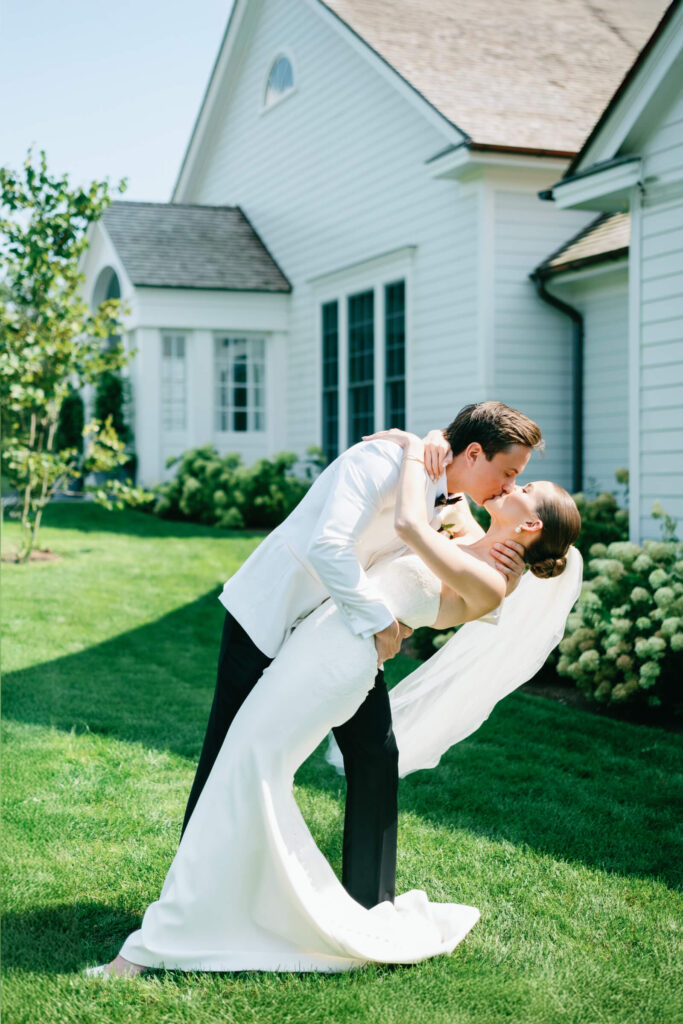 Bride and groom share a romantic dip and kiss on the lawn outside the white estate at New York Country Club