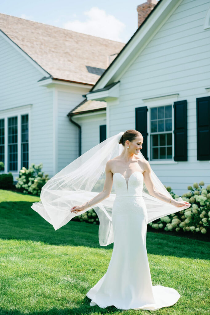 Bride joyfully twirls her veil in the sunshine on the green lawn, smiling beside the country club