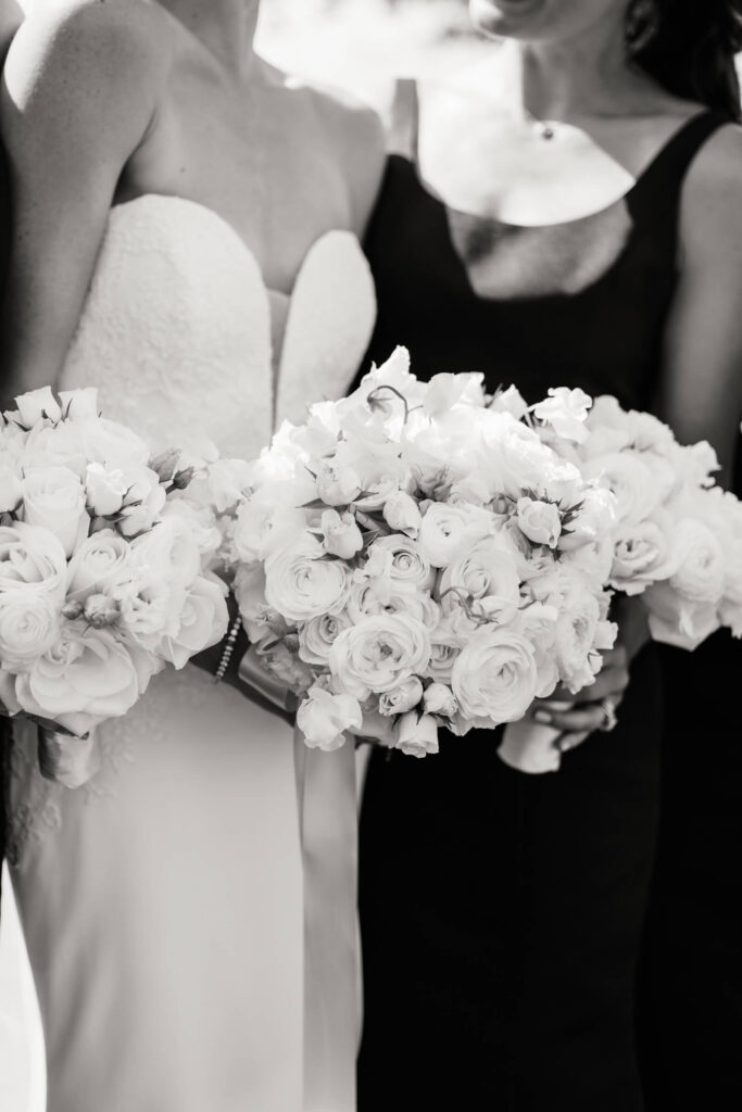 Close-up black and white image of bride and bridesmaid holding elegant white rose bouquets with delicate ranunculus