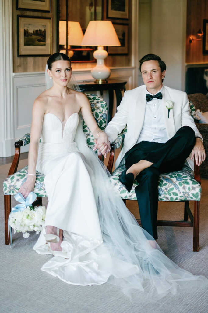 Modern bride and groom sit hand-in-hand on patterned chairs, creating a timeless portrait inside New York Country Club