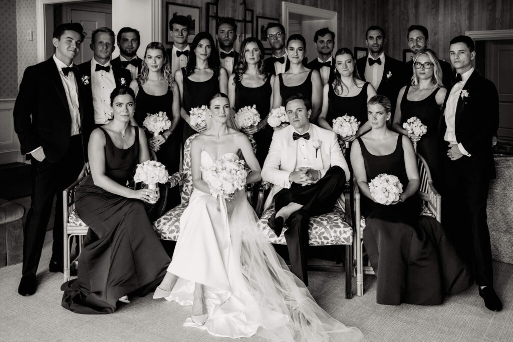 Full wedding party gathers for formal indoor portrait, surrounding the bride and groom in a classic, editorial pose