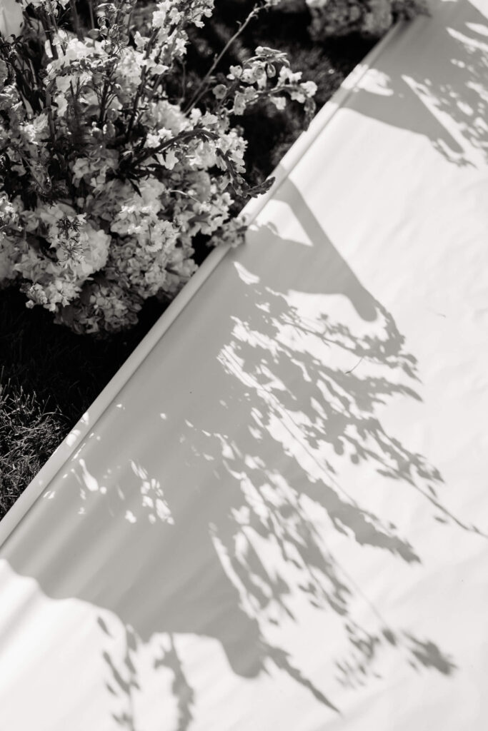 Artful shadow of floral arrangements cast on a white aisle runner during a sunny wedding ceremony at the country club.