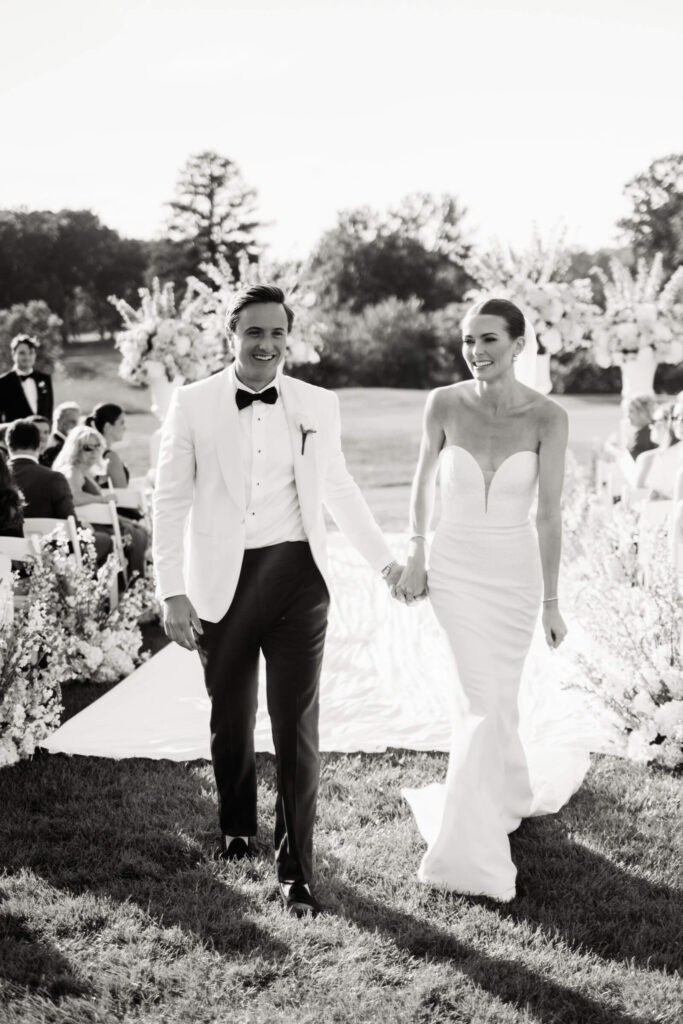 Just-married couple walks hand-in-hand down the aisle, beaming with happiness as friends and family celebrate