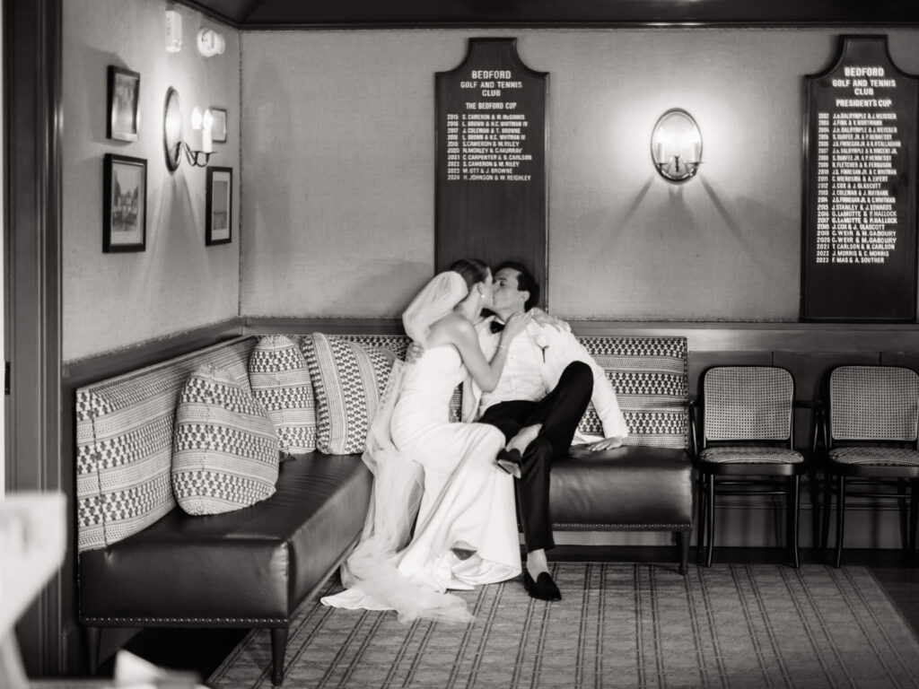 Intimate black-and-white moment of the bride and groom sharing a kiss while tucked into a quiet corner of the country club