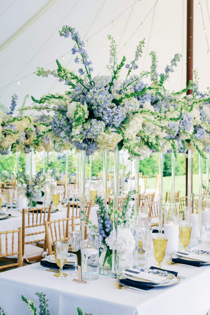 Close-up of a towering floral arrangement featuring soft hydrangeas, snapdragons, and delphiniums in shades of ivory and periwinkle blue.