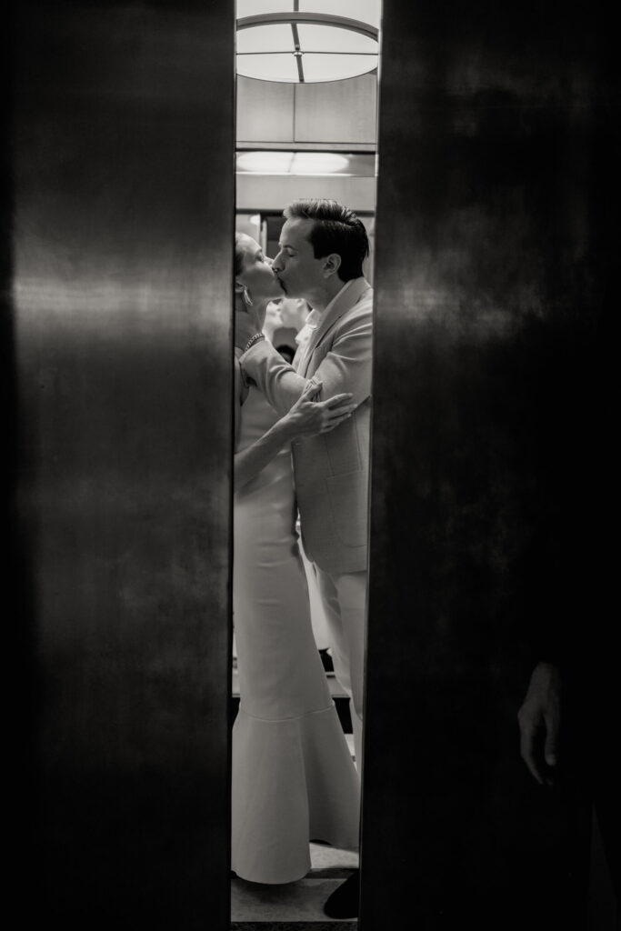 Romantic black and white image of the couple kissing inside an elevator as the doors close around them.