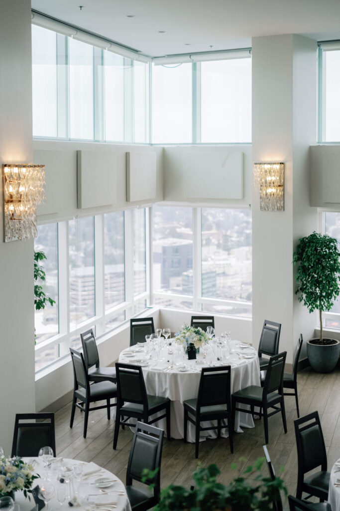 Wide view of rehearsal dinner setup at Kanopi, with guests seated around candlelit tables and city lights visible in the background.